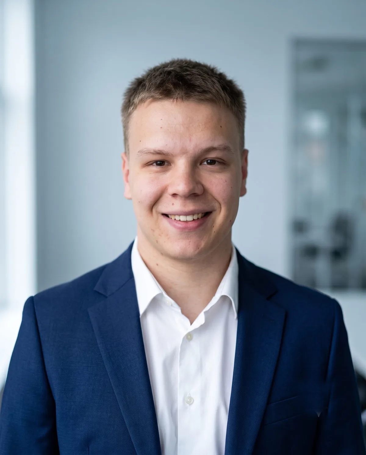 Tymon Grochowski w granatowej marynarce, uśmiechnięty, na tle jasnego wnętrza biurowego